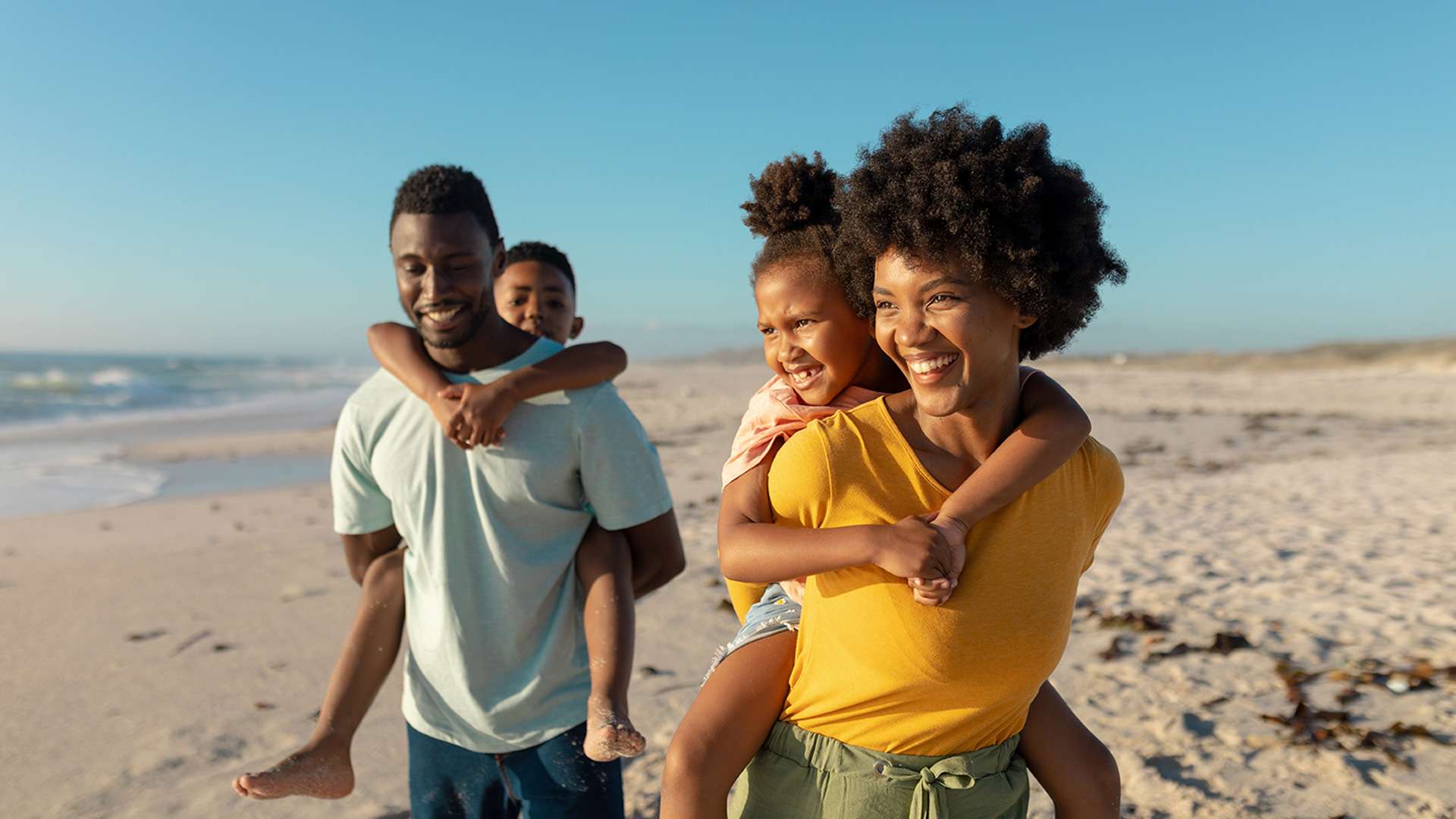 Man and woman with children on ther backs walking on beach and smiling