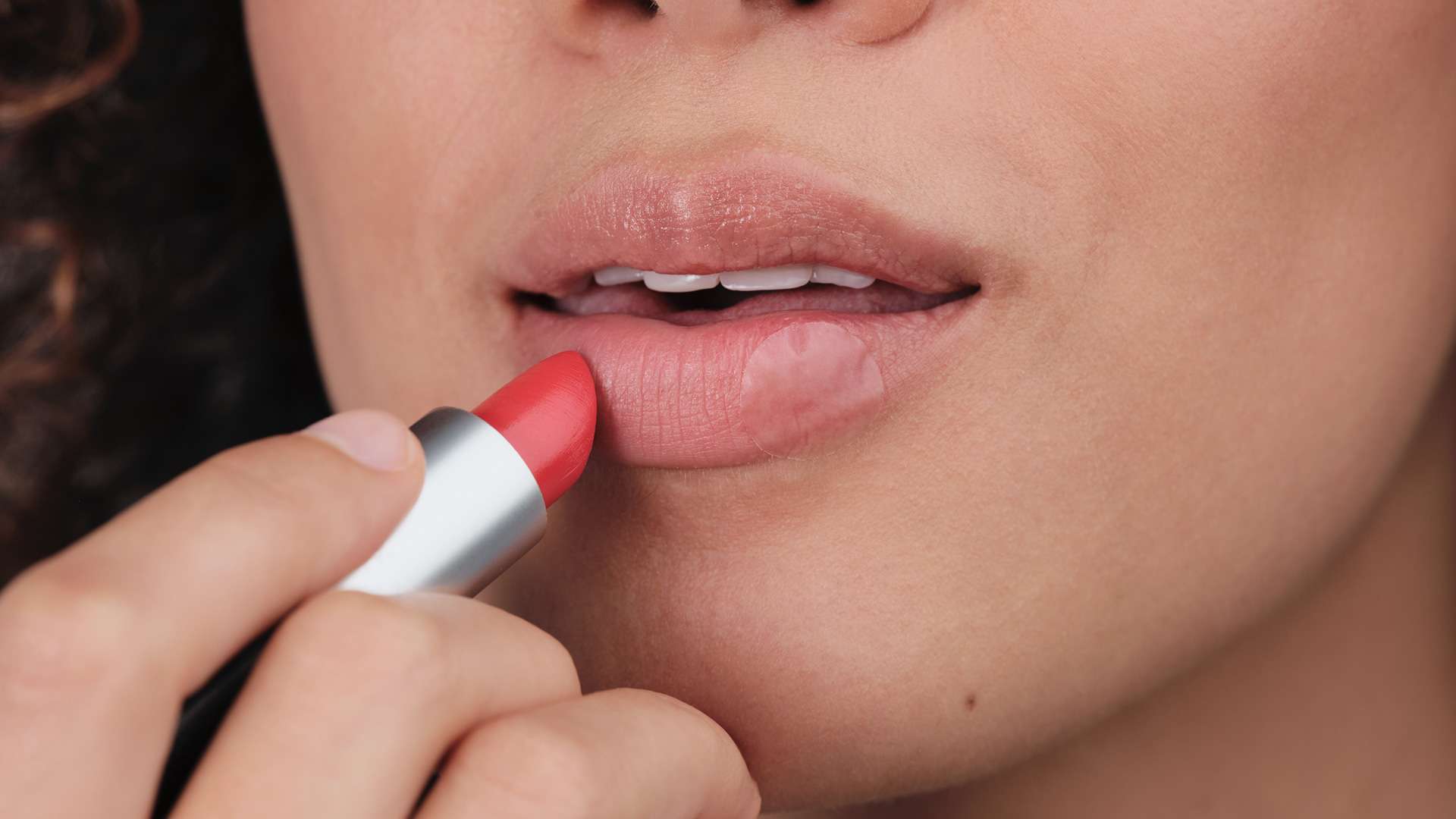 Woman putting lipstick on her lips with Herpes Patch